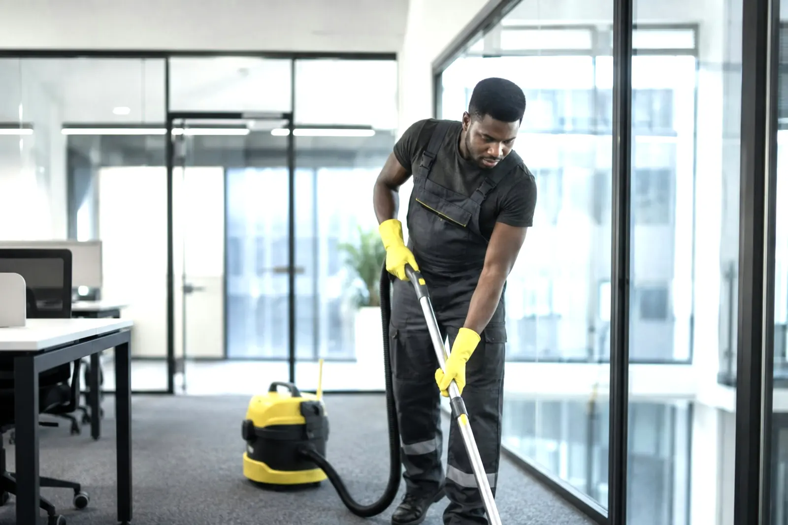 A cleaner vacuuming the carpet of a glass-walled Chicago office after hours