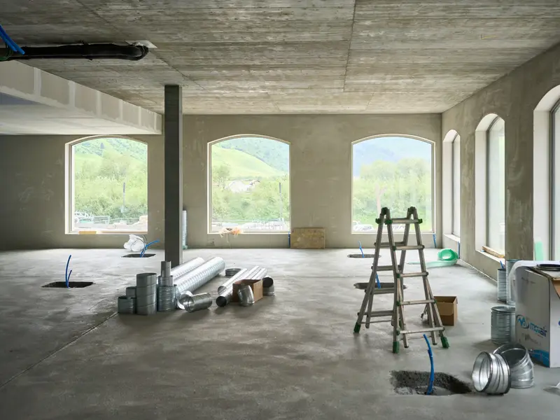 A bare concrete interior after construction, with a stepladder and materials still on the floor